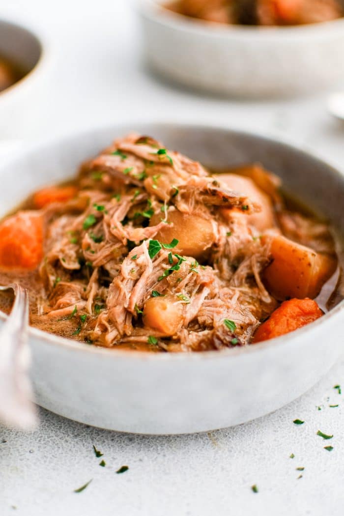 Large bowl filled with slow cooker pork shoulder with shredded pork and tender vegetables and garnished with fresh parsley.