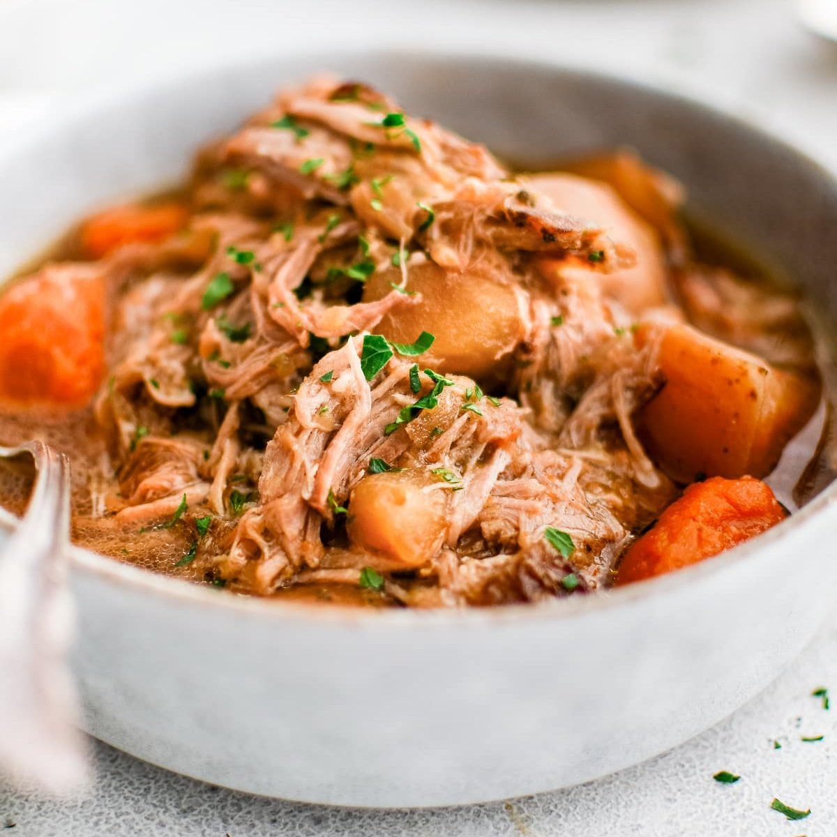 Large bowl filled with slow cooker pork shoulder with shredded pork and tender vegetables and garnished with fresh parsley.