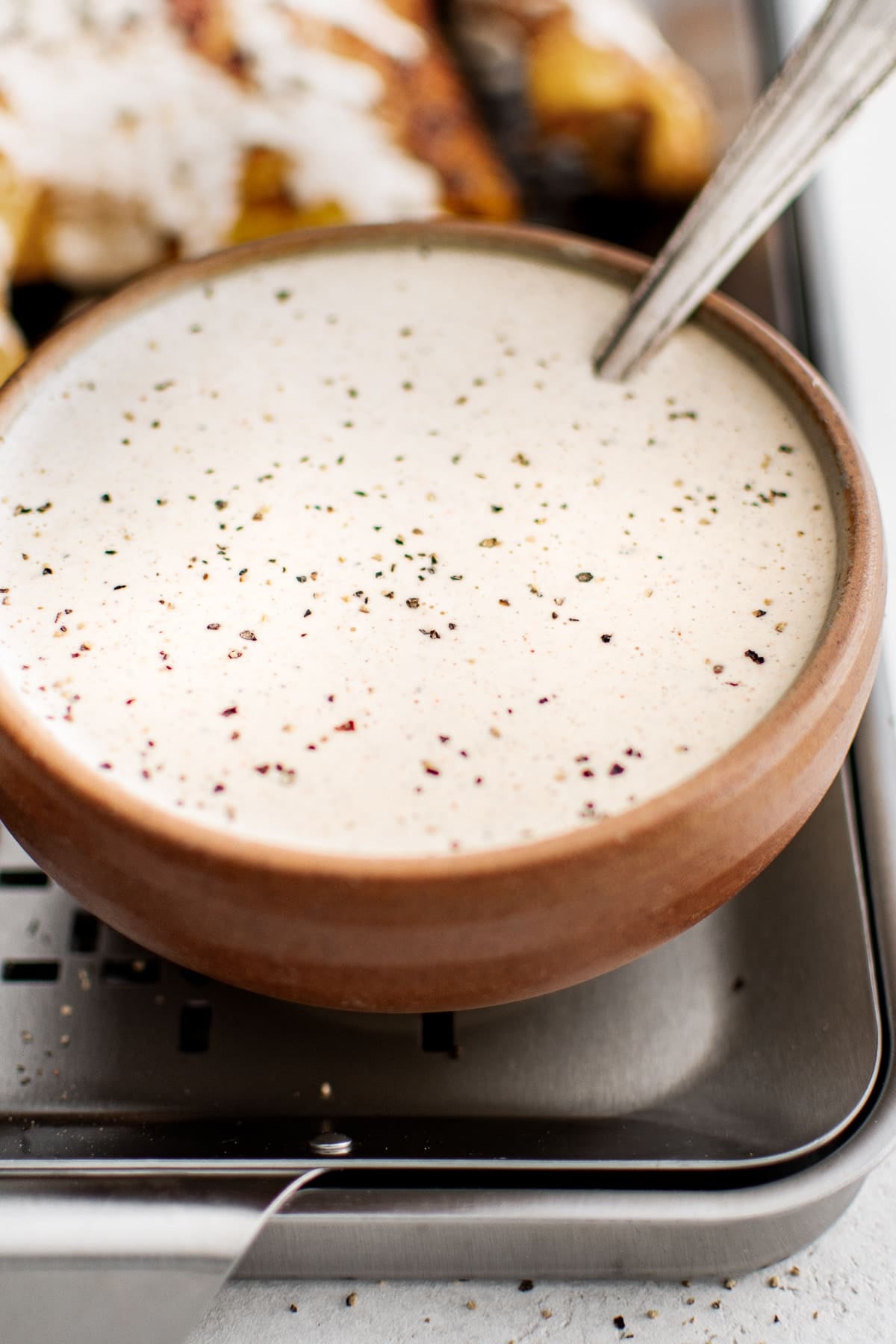 A small ceramic bowl of Alabama White Sauce on a wire rack next to crispy chicken legs.