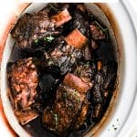 Slow cooked beef short ribs nestled in a rich red wine sauce inside a crockpot.