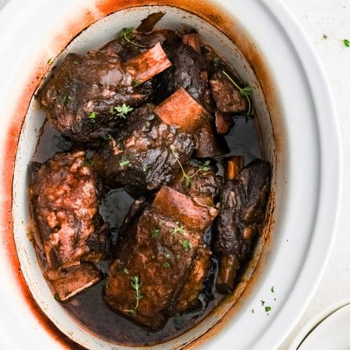 Slow cooked beef short ribs nestled in a rich red wine sauce inside a crockpot.