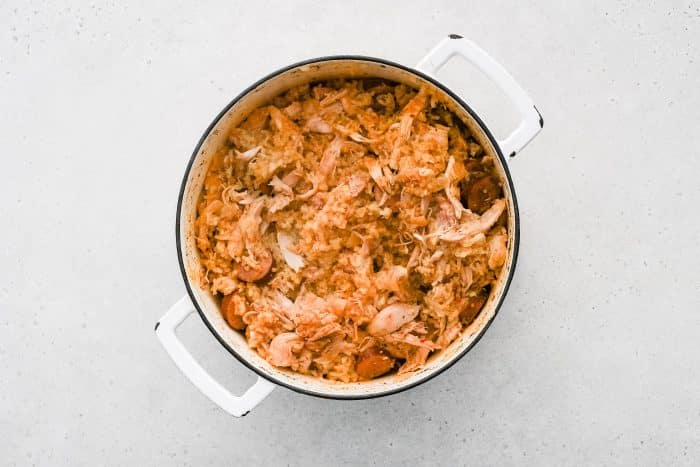 A pot filled with the finished chicken bog shows tender rice mixed with shredded chicken and slices of sausage, ready to be served.