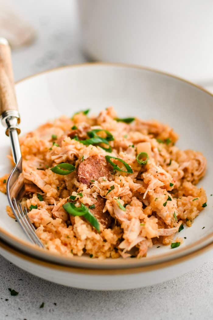 A shallow bowl filled with the cooked chicken bog shows tender rice mixed with shredded chicken and slices of sausage garnished with sliced green onions.