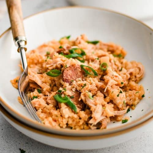 A shallow bowl filled with the cooked chicken bog shows tender rice mixed with shredded chicken and slices of sausage garnished with sliced green onions.