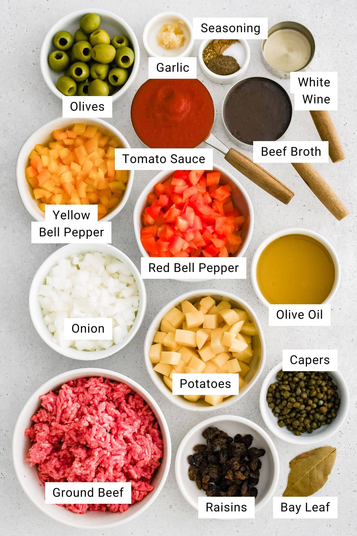 All ingredients for Cuban Picadillo with raisins, olives, and potatoes are presented in individual measuring cups and ramekins.