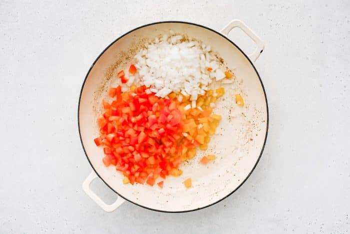 Diced onions and bell peppers sautéing in a pan.