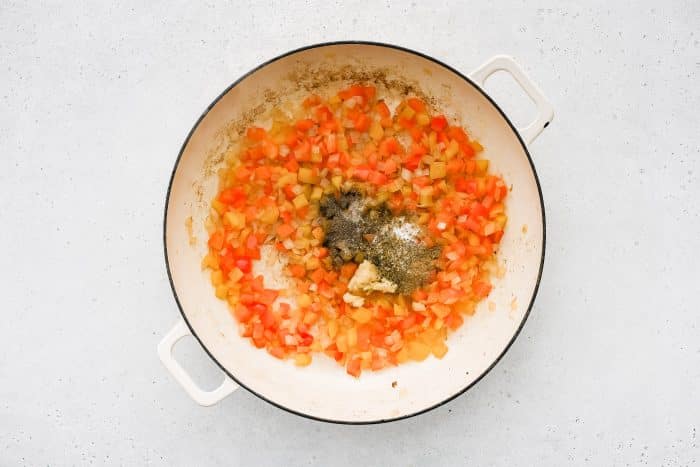 Minced garlic and spices are added to the pan with sautéed vegetables.