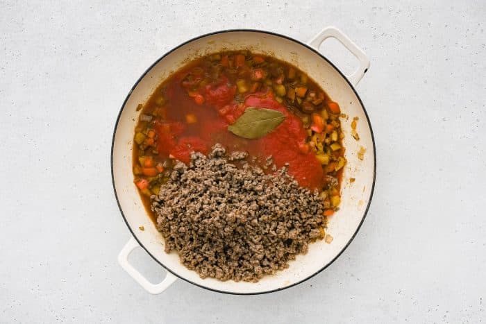 Tomato sauce, beef broth, and white wine are poured into the pan.
