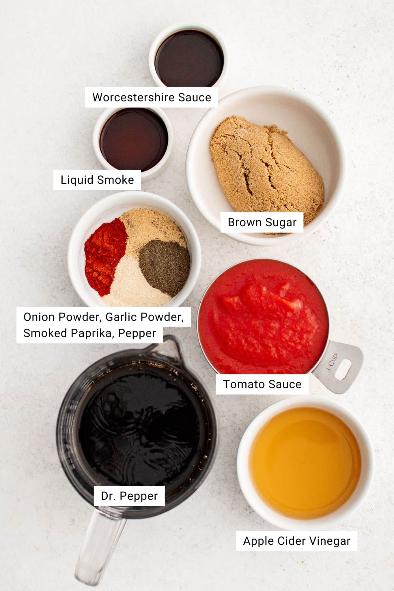 Ingredients for Dr. Pepper BBQ sauce including Dr. Pepper, tomato sauce, brown sugar, vinegar, spices, and Worcestershire sauce measured out into individual bowls ready to be used.