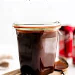Homemade Dr. Pepper BBQ sauce in a glass storage jar with a spoon set to its left and a Dr. Pepper can in the background.