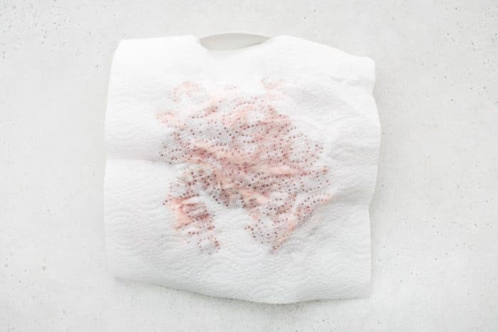 A paper towel patting a large hunk of pork shoulder dry.