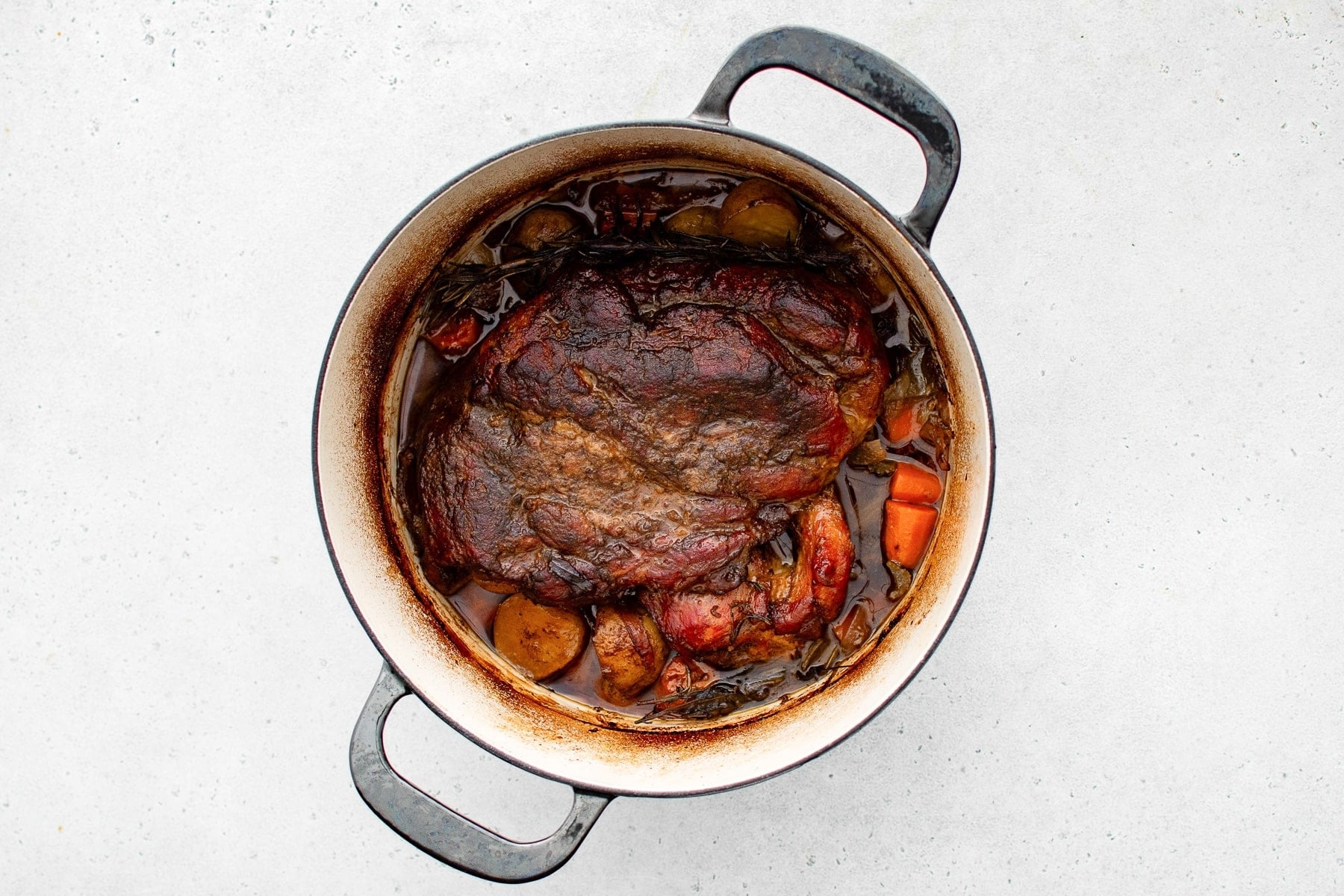 A large Dutch oven filled with a perfectly cooked fork-tender pork roast surrounded by tender vegetables.