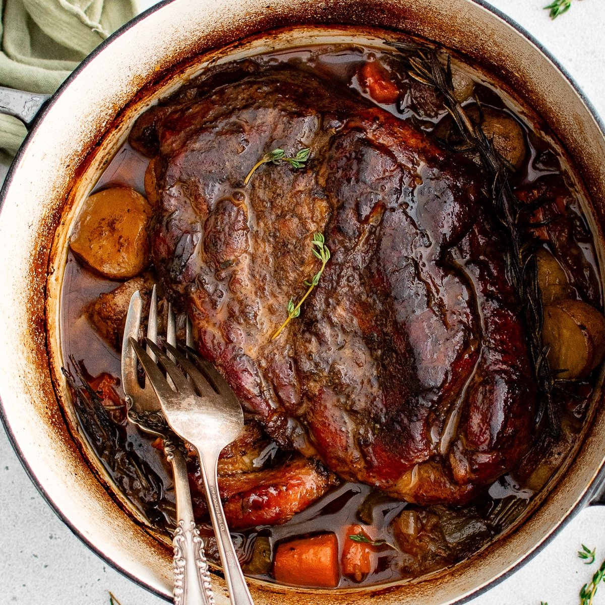 Two forks rest in a large Dutch oven filled with a perfectly cooked fork-tender pork roast surrounded by tender vegetables.