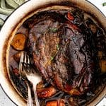 Two forks rest in a large Dutch oven filled with a perfectly cooked fork-tender pork roast surrounded by tender vegetables.