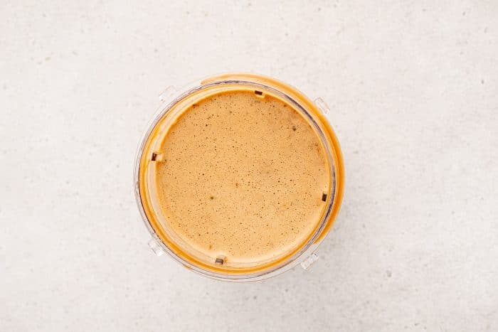 A smooth, caramel colored sauce with visible flecks of green onion and garlic shown inside the blender, freshly blended and ready for cooking.