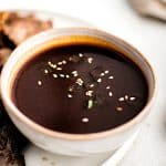 A dark, glossy bowl of homemade Japanese BBQ sauce, topped with white sesame seeds and ready to serve as a dipping sauce or glaze.