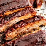 Oven-baked sliced spare ribs glazed with BBQ sauce and topped with green onions resting on a foil-lined pan.