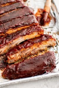 Oven-baked sliced spare ribs glazed with BBQ sauce and topped with green onions resting on a foil-lined pan.