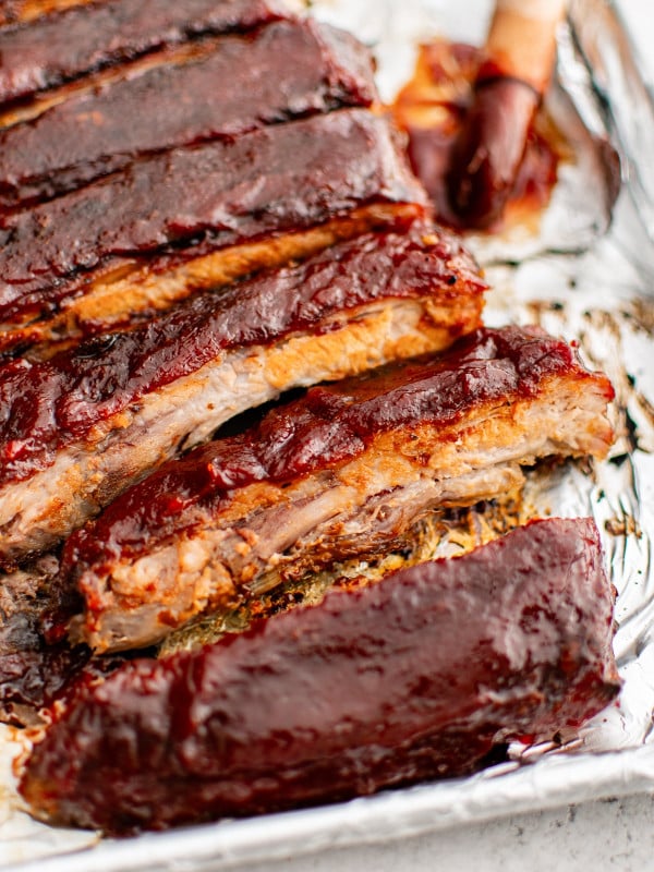 Oven-baked sliced spare ribs glazed with BBQ sauce and topped with green onions resting on a foil-lined pan.