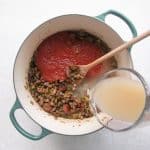 Crushed tomatoes and chicken broth stirred into the pot, forming a rich sauce.