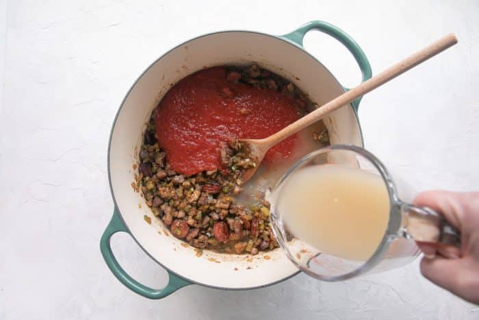 Crushed tomatoes and chicken broth stirred into the pot, forming a rich sauce.