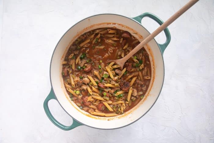 Uncooked penne pasta stirred into the simmering sauce along with green onions and parsley.
