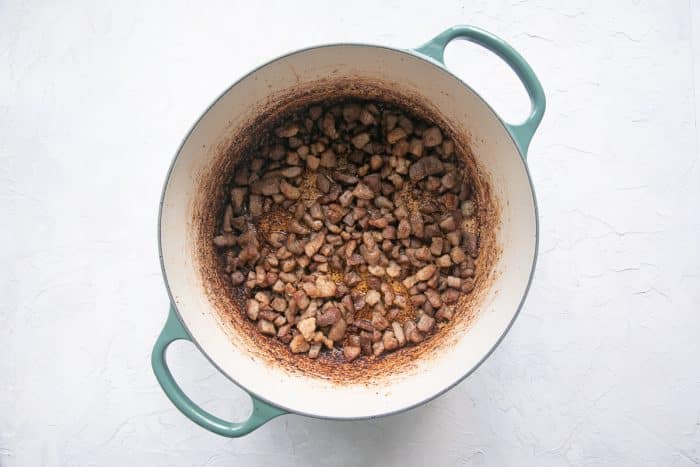 Rounds of smoked andouille sausage are sizzling in a Dutch oven, some pieces beginning to brown and crisp at the edges. A small amount of rendered fat glistens at the bottom of the pot, creating a flavorful base.