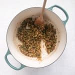 Diced celery, onion, and green bell pepper are sautéing in melted butter. The vegetables are beginning to soften and take on a golden color, while bits of fond from the meat are being lifted from the bottom of the pot.