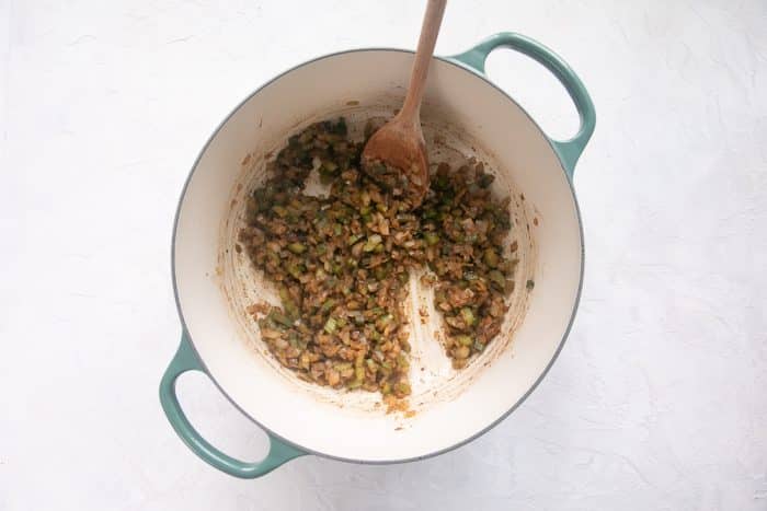 Diced celery, onion, and green bell pepper are sautéing in melted butter. The vegetables are beginning to soften and take on a golden color, while bits of fond from the meat are being lifted from the bottom of the pot.