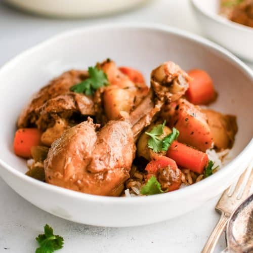 A white bowl filled with Puerto Rican Pollo Guisado served over a scoop of fluffy white rice, garnished with cilantro.