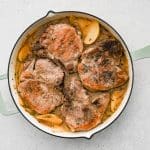 Pork chops simmering in a skillet with apples, onions, and sauce