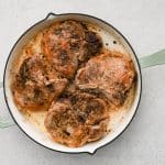 Golden-brown pork chops searing in a hot cast-iron skillet.