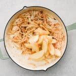 Sliced onions and apples cooking in a skillet with melted butter.