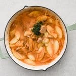 Apple cider, Dijon mustard, thyme, and broth being added into a skillet with onions and apples.