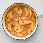Apple cider, Dijon mustard, thyme, and broth being added into a skillet with onions and apples.