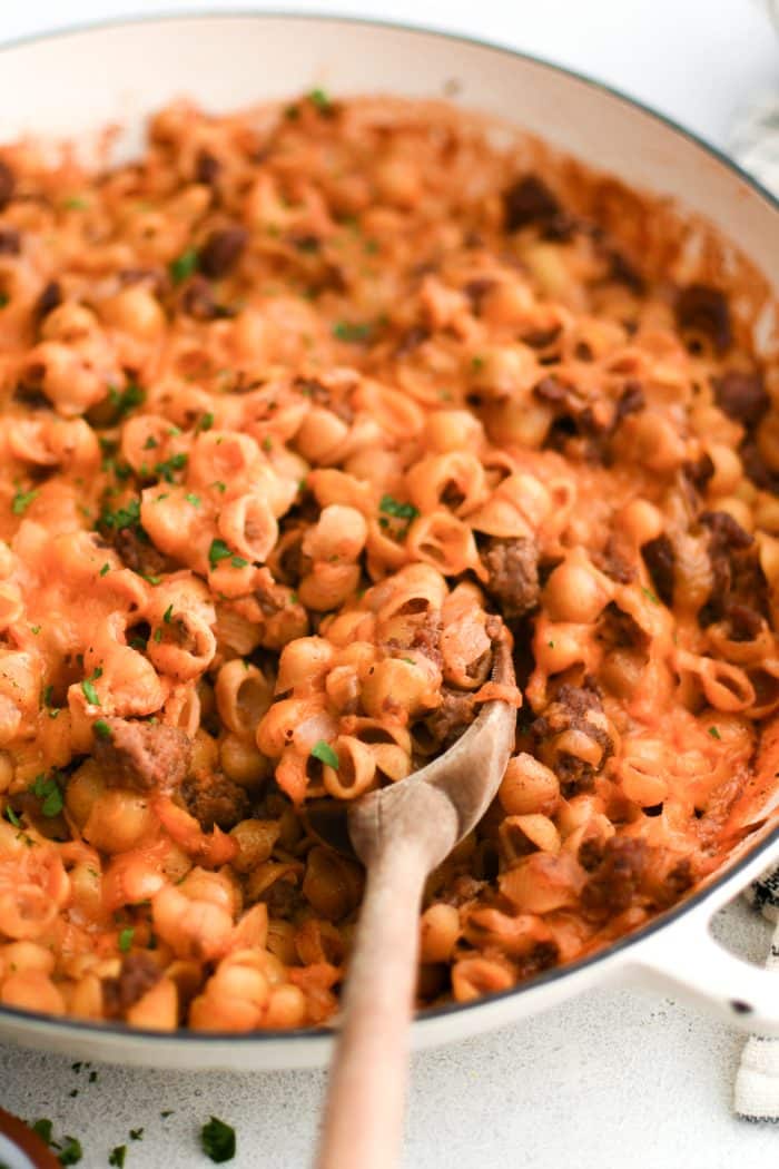 A wood spatula in a casserole dish filled with cooked sloppy joe casserole with pasta shells.