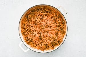 Shredded cheddar cheese is added to a large skillet filled with tender pasta smothered in a rich, tangy, beefy tomato sauce.