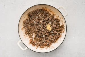 Fresh minced garlic is added to cooking ground beef and onion in a large round baking dish.