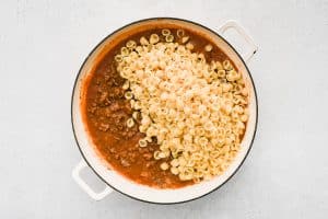 Cooked pasta shells are added to a large skillet with rich, tangy, and beefy tomato sauce.