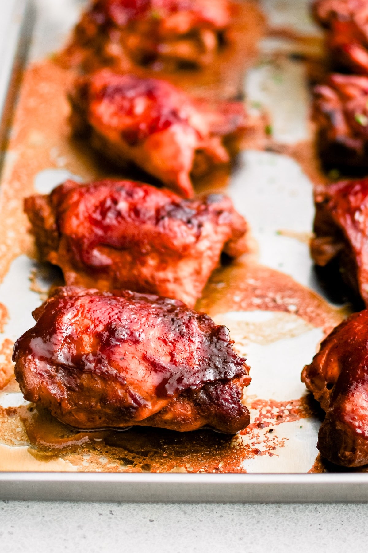A foil-lined baking sheet with slowly cooked BBQ chicken thighs covered in BBQ sauce with caramelized crispy edges.