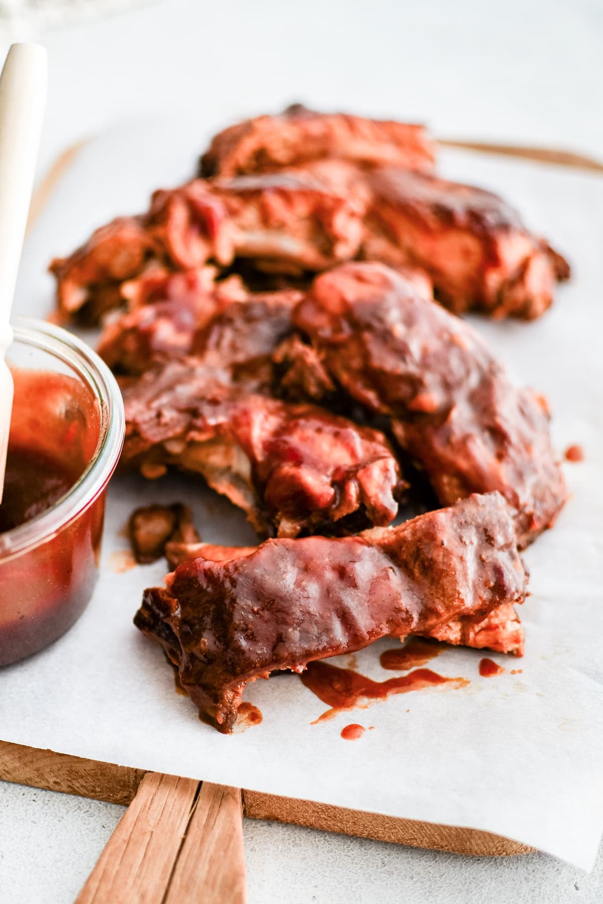 Slow-cooked baby back pork ribs on a large cutting board lined with parchment paper coated in sweet and tangy BBQ sauce.