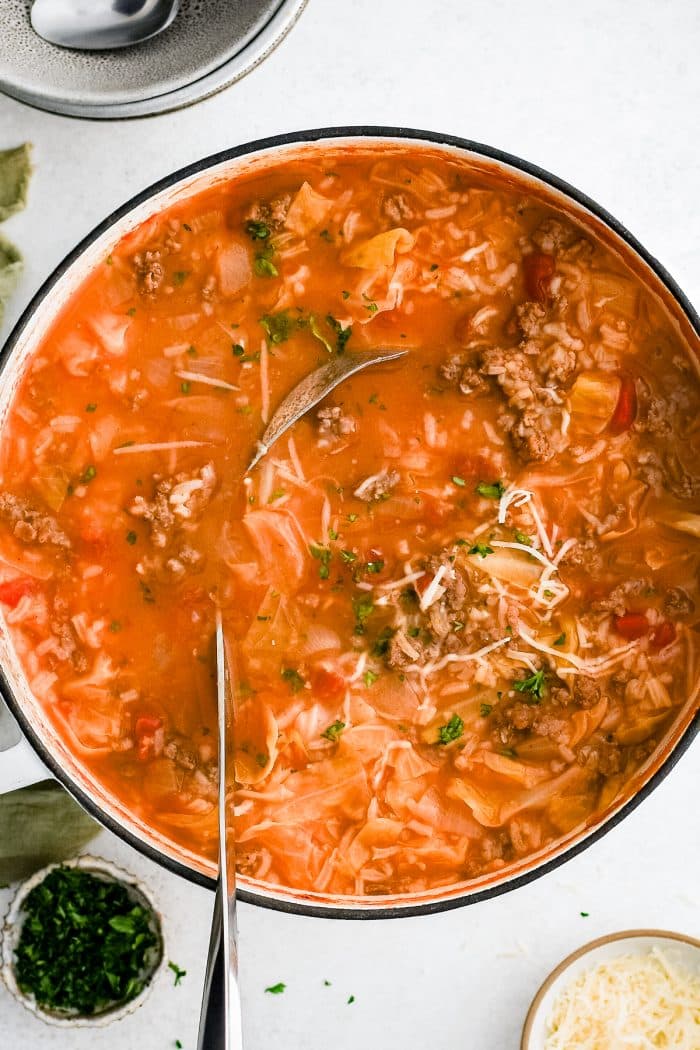 A large pot filled with steaming Cabbage Roll Soup, showing a rich tomato-based broth with chunks of green cabbage, crumbled ground beef and sausage, and soft rice.