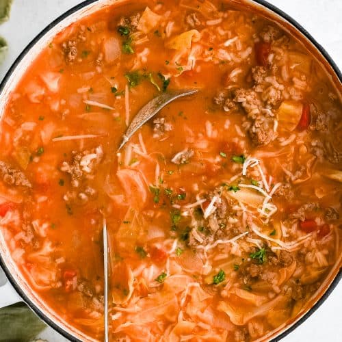 A large pot filled with steaming Cabbage Roll Soup, showing a rich tomato-based broth with chunks of green cabbage, crumbled ground beef and sausage, and soft rice.