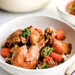 A white bowl filled with Puerto Rican Pollo Guisado served over a scoop of fluffy white rice, garnished with cilantro.
