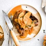 Pork chop served on a white plate with apples, onions, and sauce drizzled on top.