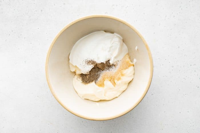 Bowl with mayonnaise, sour cream, garlic powder, salt, and pepper before mixing