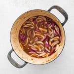 Onions and garlic being sautéed with beer and cider in a Dutch oven.