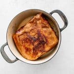 Pork shoulder searing in a Dutch oven, developing a caramelized crust.