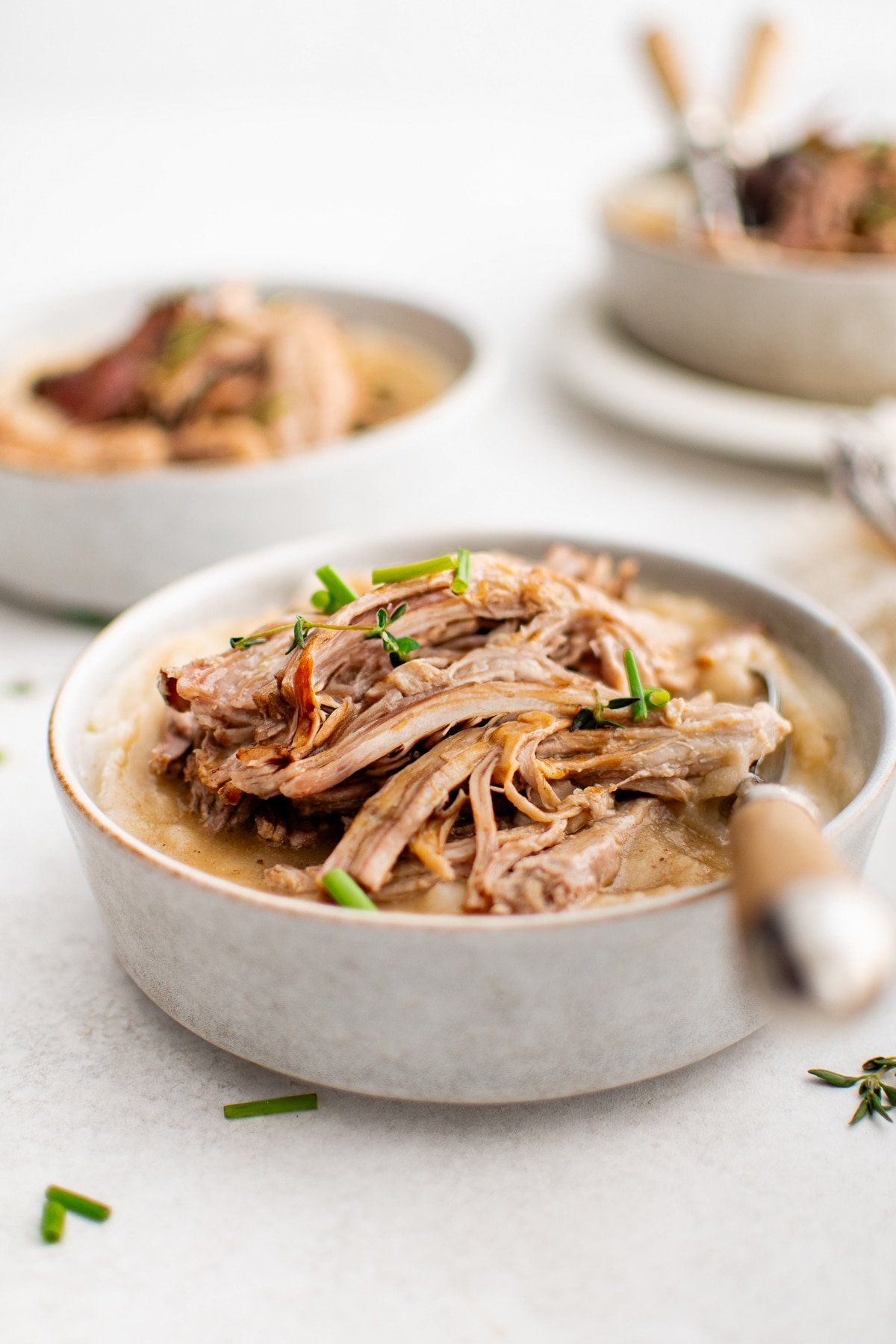 A comforting bowl of creamy mashed potatoes topped with succulent, fork-tender braised pork shoulder and garnished with fresh herbs for a rustic, hearty meal.