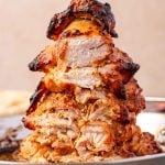 Thin slices of chicken gyro meat cut from a stack of cooked chicken gyro meat on a vertical spit.